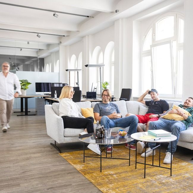 Teammitglieder unterhalten sich auf Sofas in der Lounge-Ecke des hellen Loft-Büros